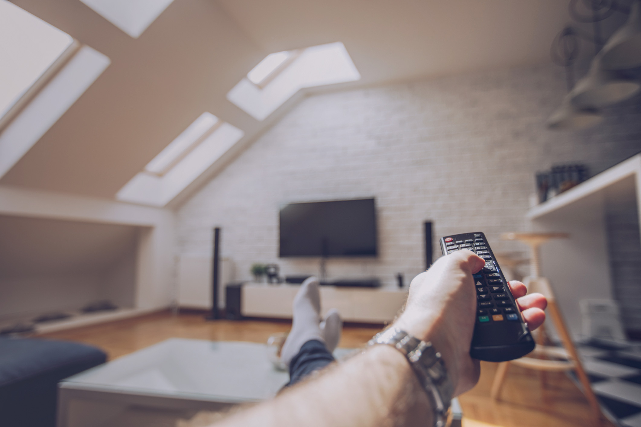 One woman, holding remote controller and watching television at home alone, cropped photo.